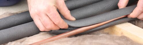 Two hands wrapping a cooper pipe with installation.