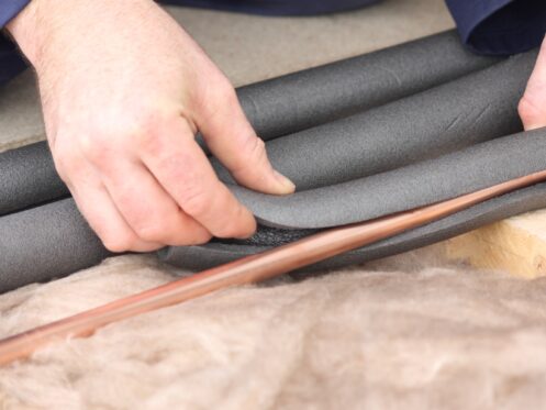 Two hands wrapping a cooper pipe with installation.