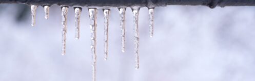 Frozen pipe outside with ice wrapped around the pipe with snow in the background