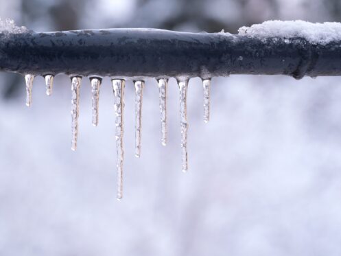 Frozen pipe outside with ice wrapped around the pipe with snow in the background