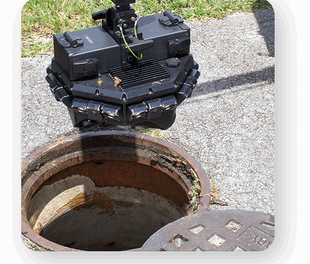 Sewer hole in the ground open with a camera set aside of the hole ready to be used